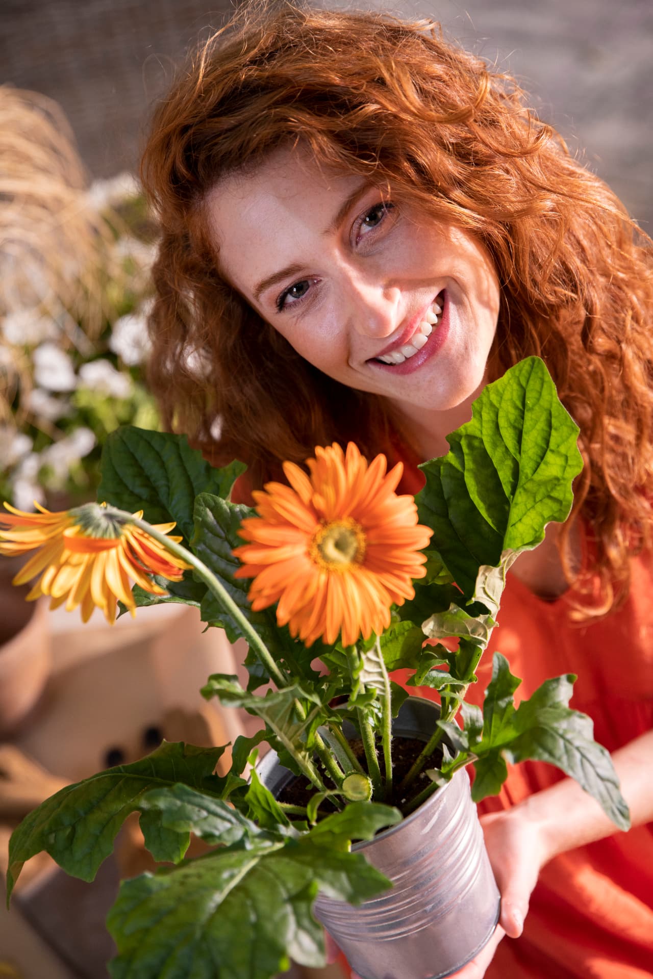 Turuncu gerbera çiçekleri tutan, gülümseyen kızıl saçlı kadın